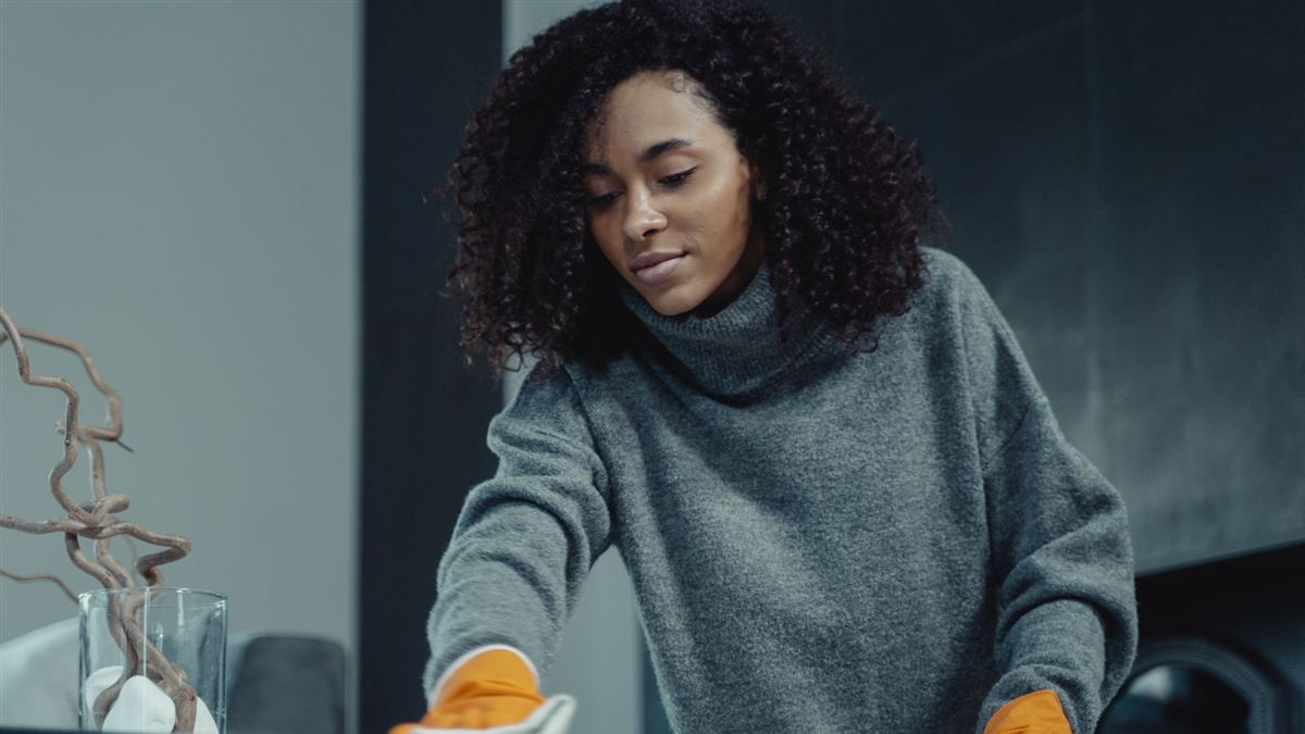Intervenante essuyant une table avec des gants de ménage dans un appartement
